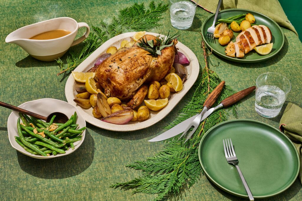 Herb roasted chicken on a platter served with green beans, gravy and a plate of sliced chicken